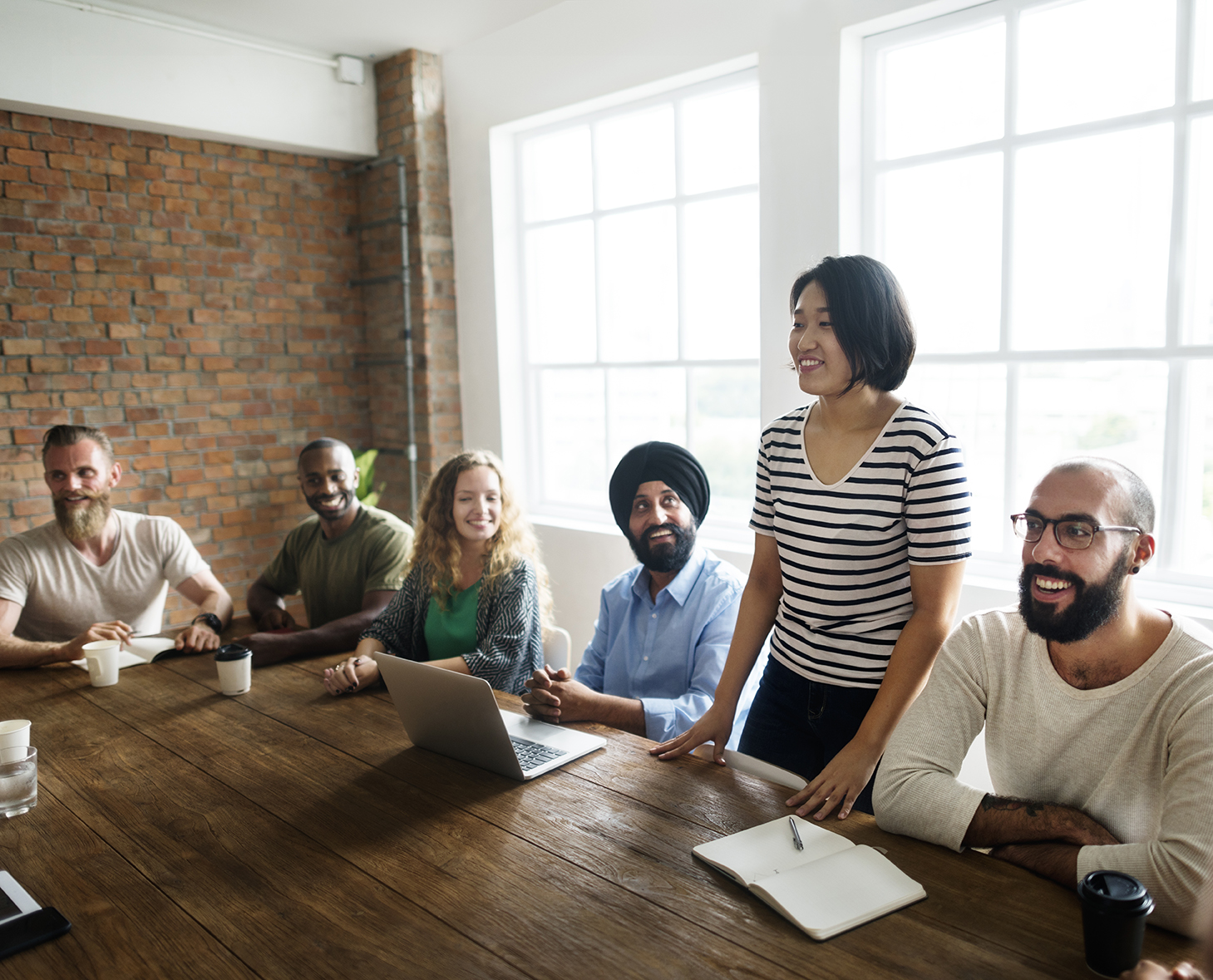 woman standing up at table in a meeting with colleagues sitting down